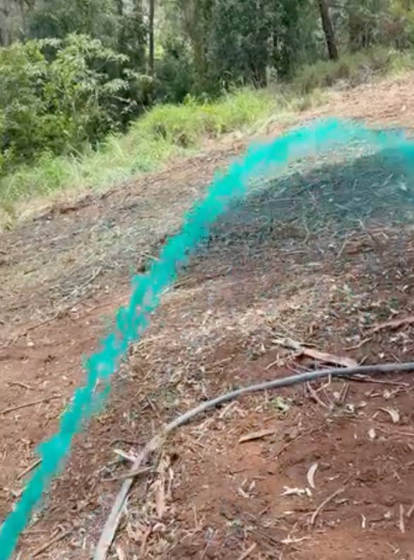 Hydroseed slurry being sprayed in a turquoise arc across freshly cleared red-earth ground, eucalypt forest in the background
